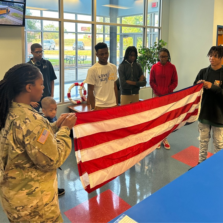 woman dressed in U.S. military uniform assists students folding a flag